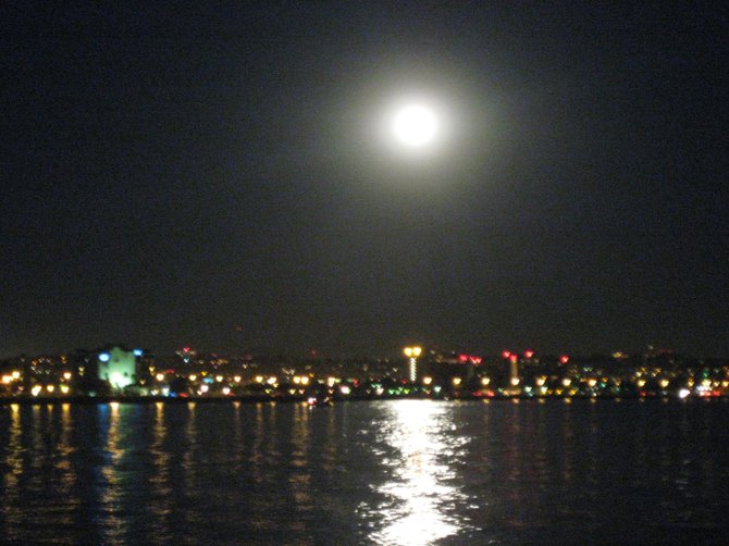 Shelter Island at night: The soft focus captures the full moon resting on the shoreline of lights still glowing

