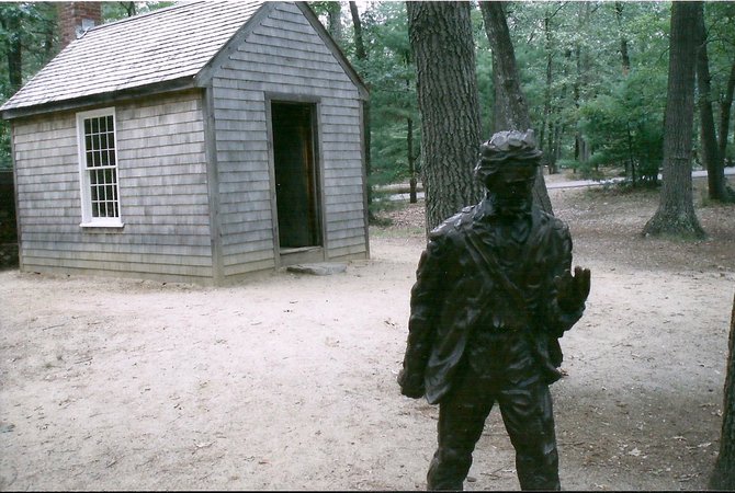 A statue of Henry David Thoreau stands before a replica of the one room cabin he built at Walden Pond in Concord, Massachusetts.