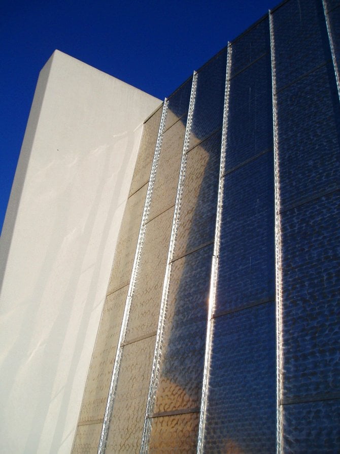 A bright white cement buttress is reflected in the sloping, shiny brushed aluminum wall of the Mission Valley Library.