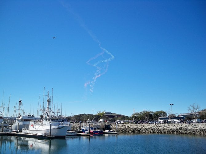 Skydivers letting out smoke trails as they glide past the Fish Market downtown.