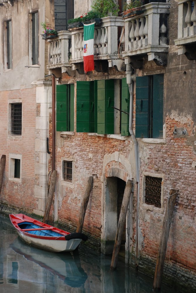 A small red boat parked along one of Venice's many small canals. It's amazing to watch as people travel by boats and canals versus cars and streets.