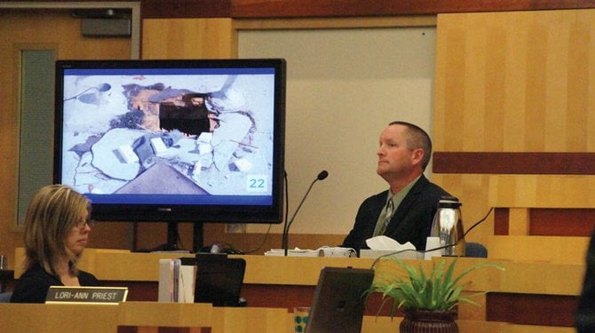 Officer Patrick Preston testifies next to a screen displaying a photo of the hole in the jewelry store’s roof.