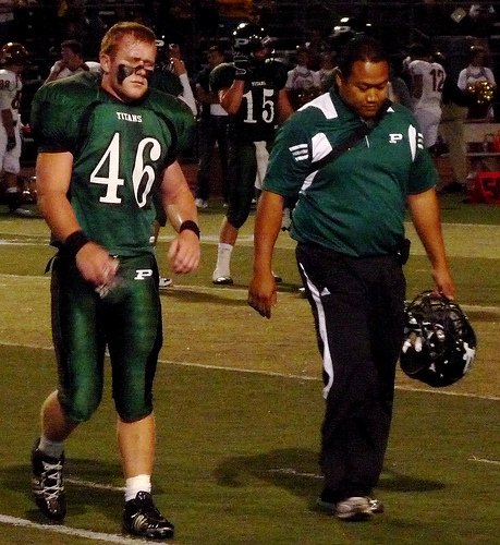 Poway linebacker Jimmy Moreno walks off the field with a team trainer after suffering an injury