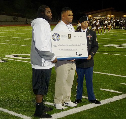 El Camino head coach Pulu Poumele (center) accepts his Chargers Coach of the Week check from Chargers defensive lineman Cam Thomas (left) and a representative from the U.S. Army