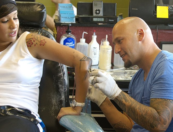 Mark Nes, the 34-year-old owner of Body Mark’s in North Park, tattoos Jessica Martinez’s elbow. 
Tattoo training, he says, would be “hard to condense into two weeks.” - Image by Alan Decker