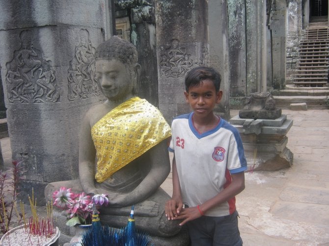 A young Cambodian poses near a statue of Buddha at the Preah Khan Temple in Cambodia.