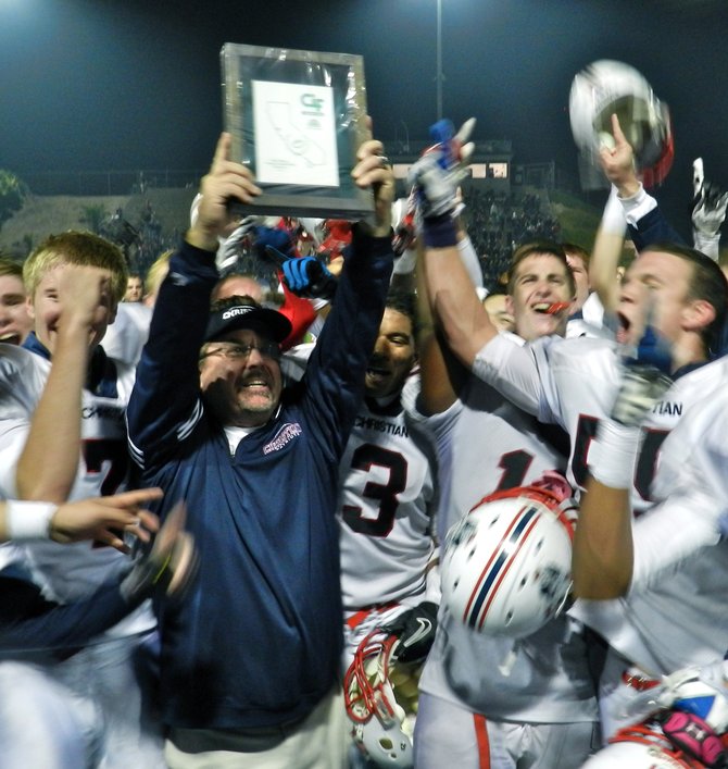 Christian head coach Matt Oliver hoists the Division V championship plaque as Patriots players celebrate around him