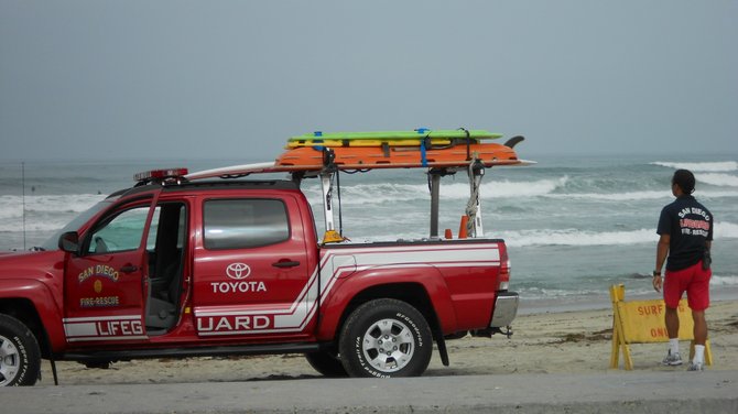 Lifeguard posting Surfing Only sign near Ocean Beach Pier.