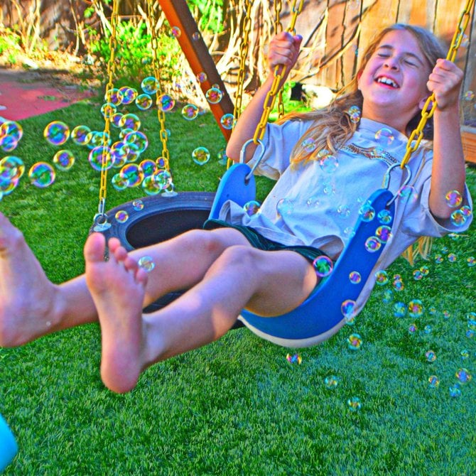 My daughter in our backyard, swinging, while my son tests out his new bubble blowing toy.