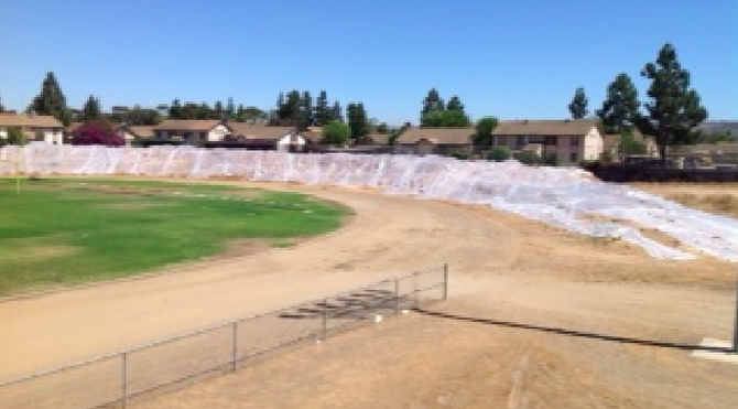 Piled dirt (covered in plastic) sits near the football field, adjacent to a condo complex