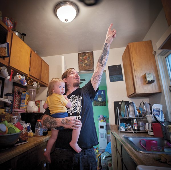 Ron “Woogie” Maggard, holding daughter, points to ceiling that leaked and got repaired in his Naragansett Avenue apartment in Ocean Beach.
