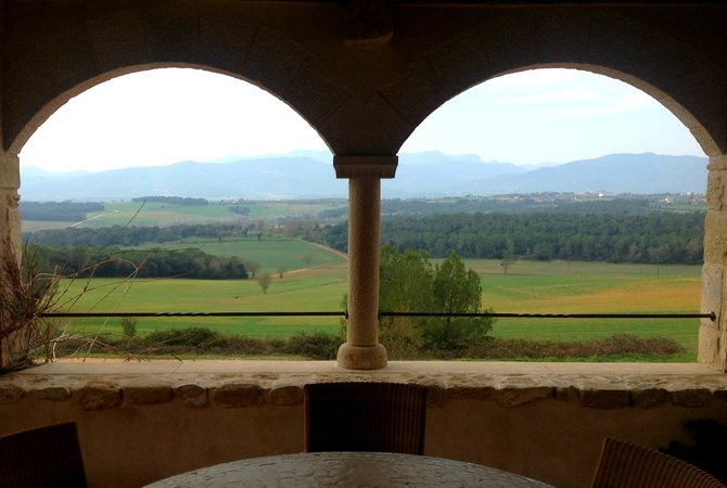 A scenic view of the snow-capped Pyrenees and La Garrotxa's volcanic hills above the terrace of the old chapel.
