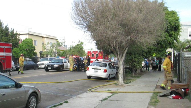 On the left, police and fire emergency personnel surround a man they had taken out of the police car and placed on the gurney; he is suspected of arson.  In the ambulance is a pregnant woman suffering from smoke inhalation.  On the sidewalk are the residents of the home what was set on fire, being interviewed by the police officer off to the right.  A firefighter is seen entering the property, in front of which is the injured man's belongings which were thrown out by the man's girlfriend.