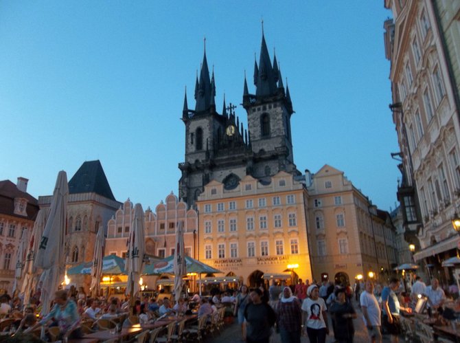 Týn Church rises up behind Old Town Square at dusk. 