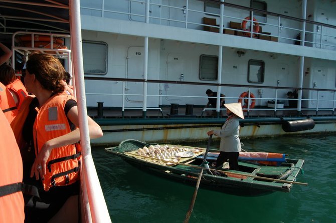 Peddler wearing nón lá (leaf hat) sells her wares on a sampan to the ship's passengers.
