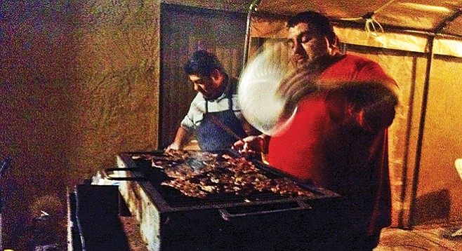 César fans the coals under his rack of carne asada
