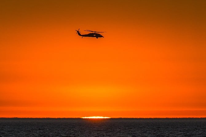 A Navy SAR helicopter aligns with the setting sun at Silver Strand State Beach.