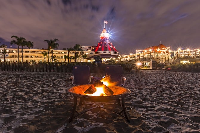 A stormy moonlit sky over the Del Coronado. A fire pit and outside seating is setup on Del Beach for hotel guests.