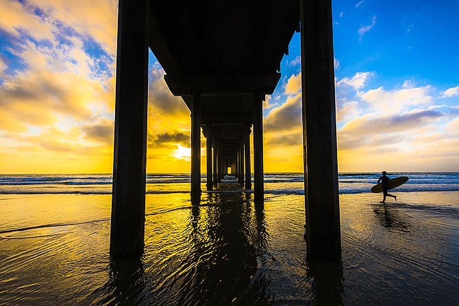 A surfer running through the water to catch the last waves at sunset.