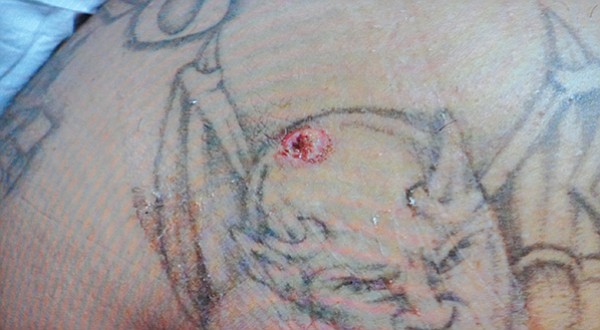 Bullet hole in tattoo of Satan’s head, on Nico’s back shoulder
