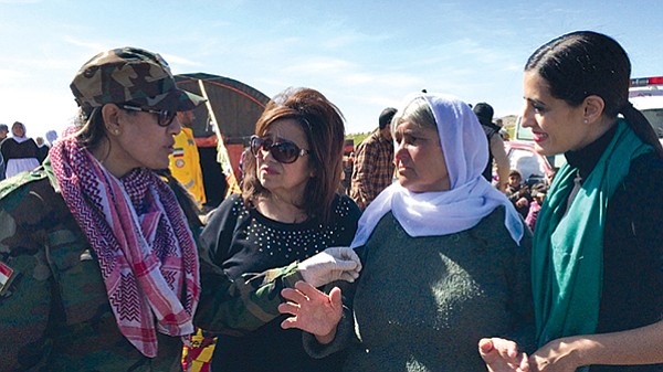 L-R: An unknown soldier of the Kurdish female fighting units explains to Yvette Isaac the challenges of protecting the Yazidis from ISIS; to Isaac’s right are an Yazidi elder and daughter Jacqueline.