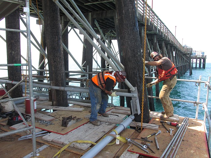 Work crew aligning and pounding in bolts to support crossbeams 