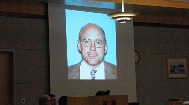 See defendant Jeff Barton seated below photo of himself displayed for jury.