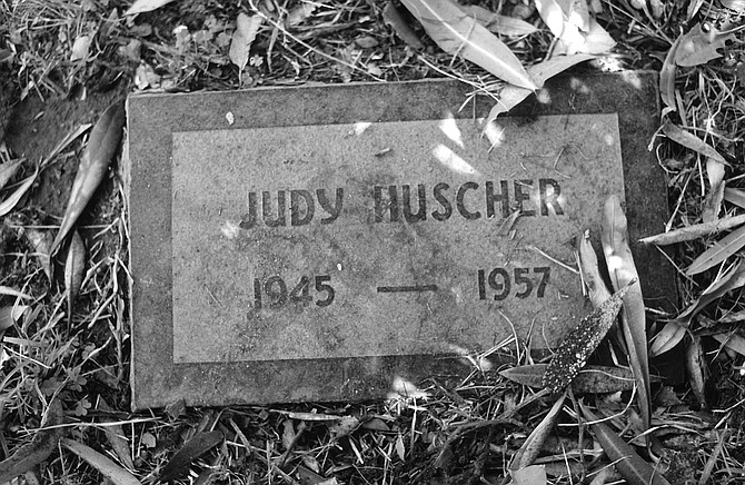 Judy’s stone, which says simply “Judy Huscher, 1945–1957,” sits between Hank Decking and an oleander tree, whose long, poisonous leaves make flickering shadows on her name. 