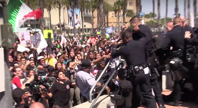 A man in a white T-shirt and black ballcap (center) falls back after police thwart his attempt  to scale a barrier separating protestors from rally attendees at the San Diego Convention Center. A Mexican flag waves in the background. Upon hearing of the fracas, Trump quipped: "I guess it’s a good thing I’m not running for president of Mexico. And maybe if we’d had a better wall in place, the conflict could have been avoided.”
