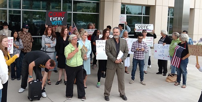 Martha Sullivan and Ray Lutz lead a crowd of protesters outside the county registrar