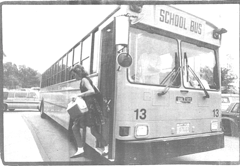 A woman with a red scarf tied over her hair hoisted what must have been a six-year-old boy onto he first step of the school bus.