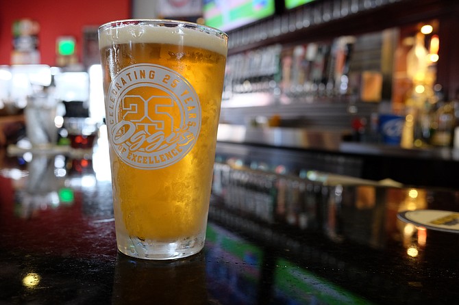 A pint of Oggi's orange wheat anniversary beer sits on a bar during a baseball game.