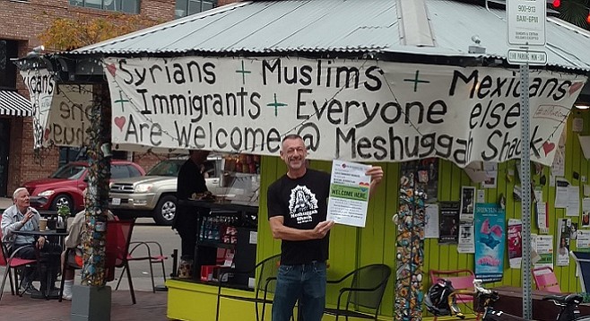 John Bertsch displays a flyer along with handmade signs at the Mission Hills Meshuggah Shack