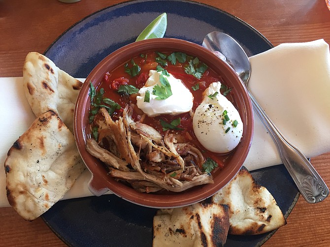 The Shakshuka is a Middle Eastern breakfast dish featuring eggs poached in a broth of tomatoes, peppers, onions and white beans. Madison serves it with carnitas on top.