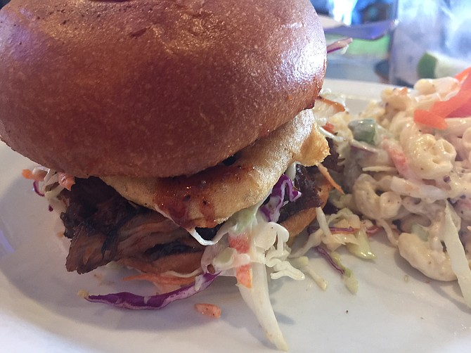 The pulled-pork sandwich is topped with homemade slaw, a large onion ring, and a brioche bun. 
