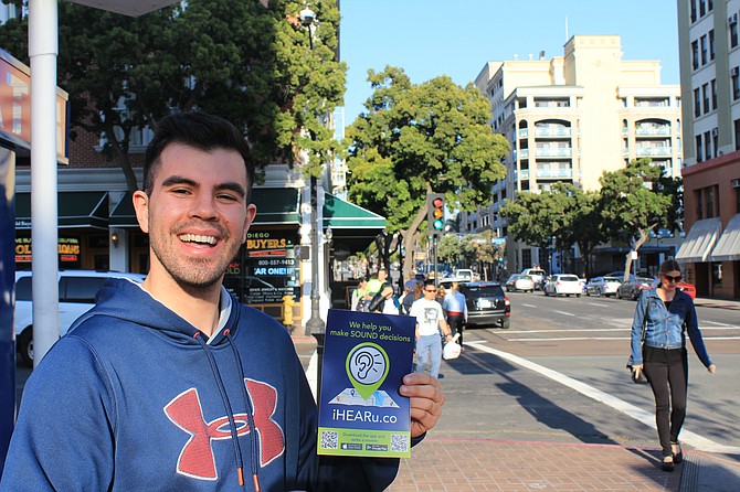 Evan Soto holds an iHEARu window sticker before reviewing a restaurant in the Gaslamp Quarter of San Diego.