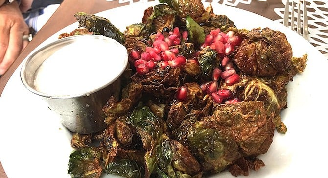 Fried Brussels Sprouts covered in fresh pomegranate seeds and served beside a heaping portion of tangy and spicy yogurt