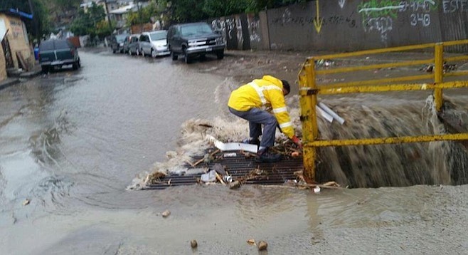 A city worker attempts to clear a storm-drain grate