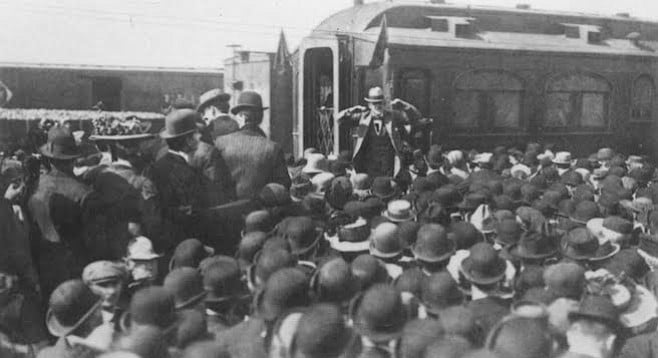 Eugene Debs speaking before a crowd next to a Pullman train car, the manufacturer of which was a strike target due to unfair treatment of workers.