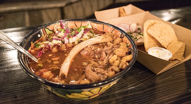 The meat has fallen off this baby back rib bone, into the pozole soup.