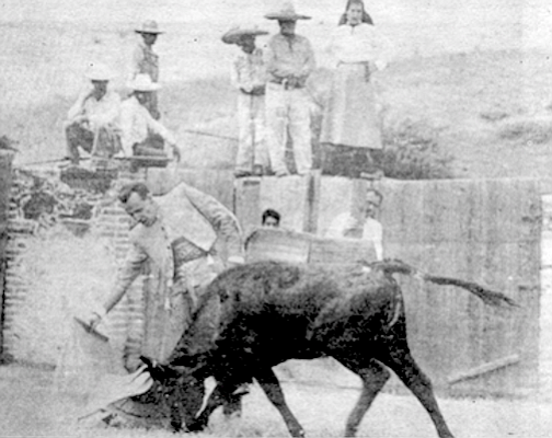 John Wayne peeks out from behind post as Boetticher demonstrates guiding a bull with a muleta.