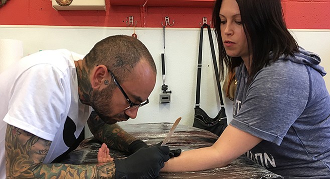 Phil Mayhew touches up Sarah Kahn’s arm tattoo at Primos Tattoo in Escondido