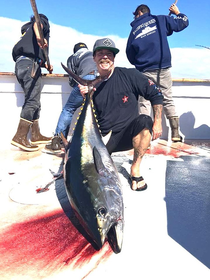 Angler poses with 100-lb-class bluefin tuna while Pacific Queen crew readies the gaffs for another.