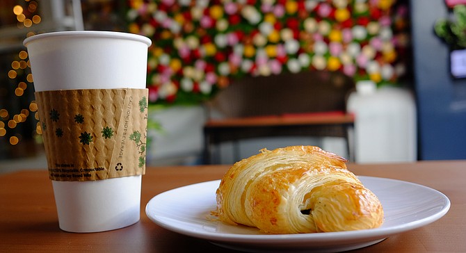 A coffee and croissant, with a wall of roses for background