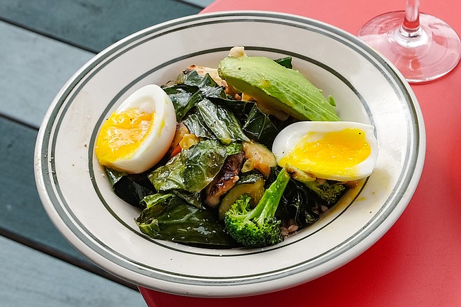 A breakfast bowl of farro topped with braised collard greens, roasted vegetables, soft-boiled egg, and avocado