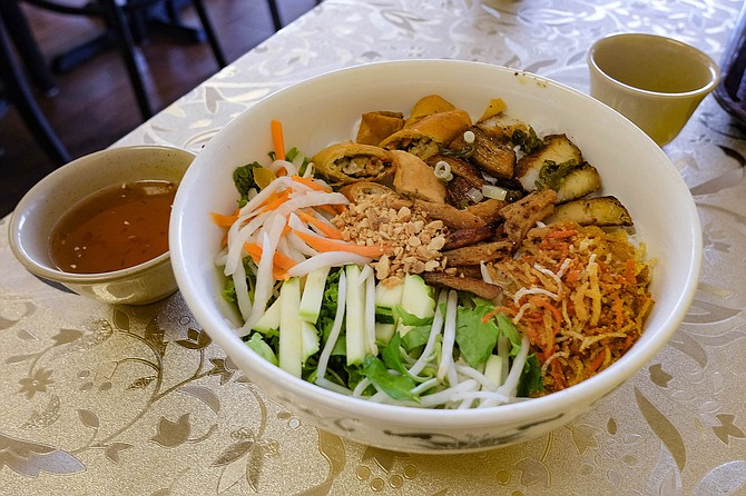 Cold vermicelli noodles topped with a mix of vegetables, faux meats, crushed peanuts, and chopped egg rolls