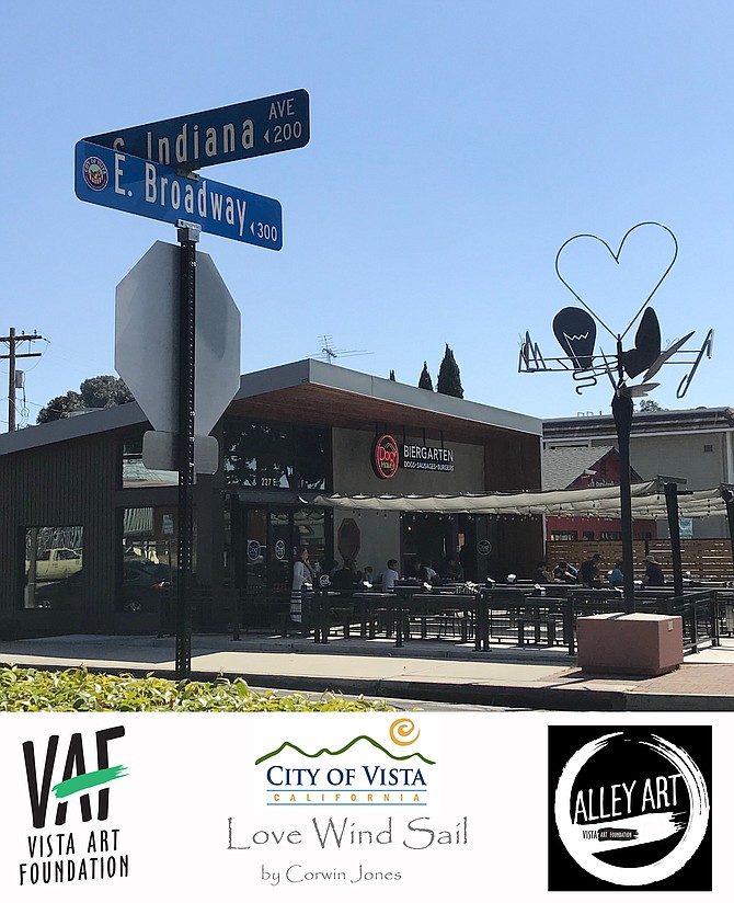 On Friday May 3rd, 2019 we attended the City of Vista’s latest unveiling of alley artwork designed to dress up a revitalized downtown district area to include creative works of art from local artisans. The city’s “Kites over Vista sculpture initiative” is meant to provide pedestrians a thought provoking experience by positioning creative design pieces within the city center sidewalks and meeting areas within the heart of the city. We had to chance to interview the talented young artist Corwin Jones of Vista, CA who created the art piece appropriately named  “Love Wind Sail” to understand his inspiration and meaning for the creation.

Corey stated “I drew several points of inspiration and passion from my life to fuel the final design that you now see here today”.  “The concept of the wind sail is to portray love through the actions we make to fulfill our soul”. “The heart acts as a center piece while representing the mind, body and spirit working as one”. “The butterflies represent a connection made between two individuals”.   “Light bulb brings the bright dignified ideas of the mind”. “The mountains express one’s lust for nature, whereas the musical note represents the importance of art and self-expression in one’s life”. 

The beautifully hand-crafted all metal piece stands roughly 15 feet off the ground and is perfectly balanced to rotate horizontally even with the slightest bit of wind.  Its an excellent example of a modern minimalist metal design coupled with ecstatically pleasing kinetic motions. The new art piece can be found on the corner of East Broadway and Indiana streets, right next to the newly opened Beirgarten restaurant.

A very interesting video was taken of the actual installation process to commemorate this intriguing new art piece, the URL is  https://vimeo.com/334080419