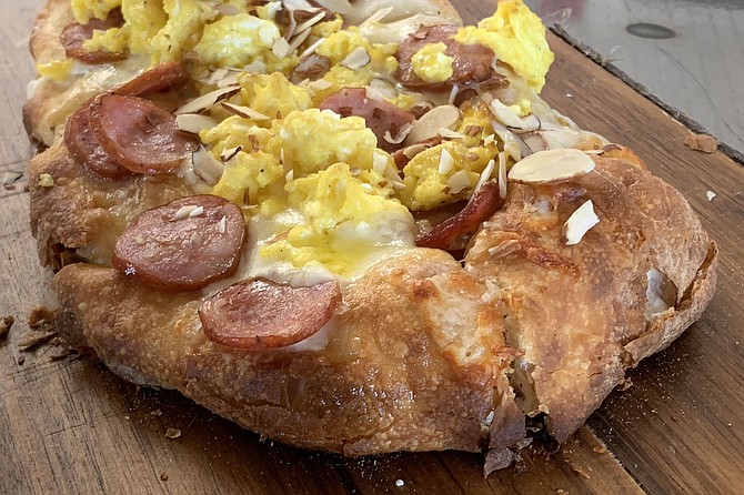 Breakfast pizza with sausage, provola cheese, scrambled eggs, and slivered almonds