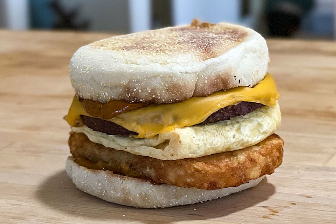A vegan breakfast sandwich, with plant based eggs, sausage, and cheese, plus air-fired hash browns and maple chipotle sauce