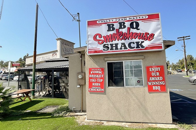 A small BBQ shack stands in front of a grocery parking lot.